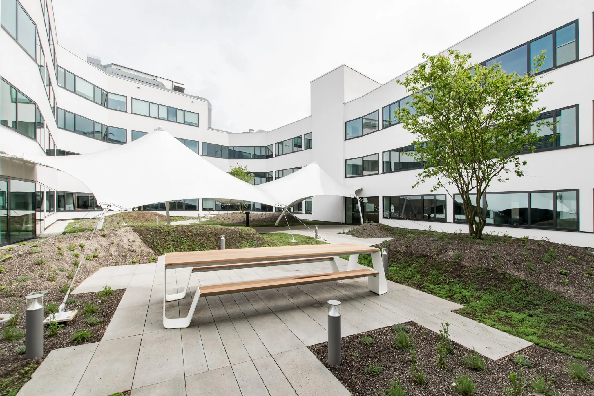 Binnenplaats van een modern kantoorgebouw aan de Grote Marktstraat met zitbanken, witte zonneschermen en aangelegde tuin.